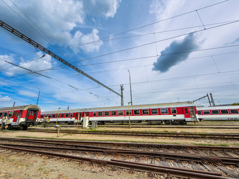 Red passenger train carriages sitting on railroad tracks at depot. A low angle photograph captures train cars parked along steel tracks under blue sky.