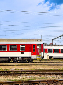 Red train carriage with open door on tracks. A red passenger train wagon with an open door sits on tracks under overhead power lines and sky.
