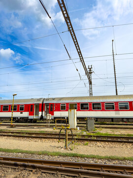 Passenger train carriages parked at railway yard. Red passenger train carriages stand on parallel tracks near an overhead electric mast during daytime.