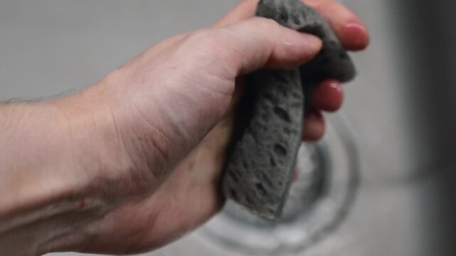 A soapy dish sponge in a man's hands.
Water drips from a soapy gray dish sponge.