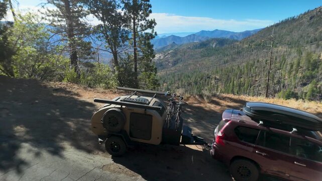 SUV pulls a teardrop camper trailer on the road to Sherman Pass in the Sierra mountains, surrounded by tall trees and mountains.