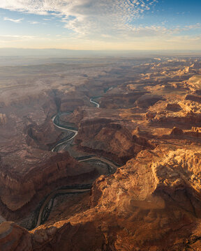 Aerial view of the winding Dirty Devil River cutting through the rugged red rock canyons of the desert landscape under a soft morning sky in Garfield County, Utah, United States.