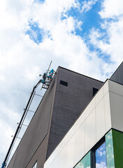 Aerial boom lift reaching top of building wall. Hydraulic cherry picker elevates worker to upper facade edge under blue sky with scattered clouds. © Анна Терелюк