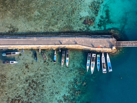 Aerial view of Karimun Jawa island with a long concrete pier, wooden boats, and clear coral reefs in the turquoise water in Karimunjawa, Central Java, Indonesia.