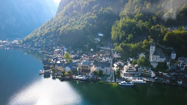 Aerial Drone Pullback and Rising Reveal of Historic Hallstatt Village with Iconic Churches, Alpine Houses and Lake Hallstatt in Austria