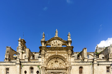Intricate Baroque and Gothic facade details of the historic Iglesia Mayor Prioral church in El Puerto de Santa María, Spain, featuring religious sculptures under a clear blue sky © photoopus