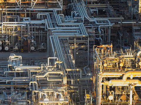 Aerial view of an oil refinery featuring a complex network of industrial pipes, metal scaffolding, and steel structures illuminated by golden hour light in the United Kingdom.