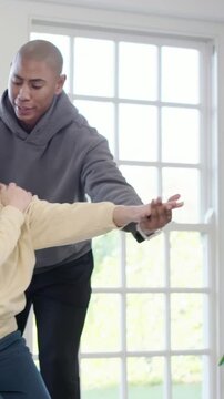 Vertical video: Leaning caregiver guiding senior through arm stretches for mobility near window