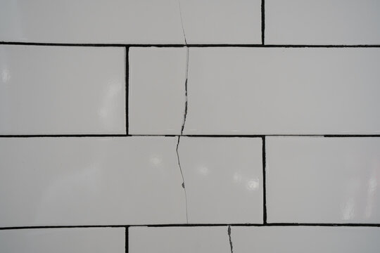 Long fracture runs through white bathroom tiles installed over uneven wall, showing poor surface preparation, hollow spots, adhesive failure, tile detachment risk and costly home renovation problem.