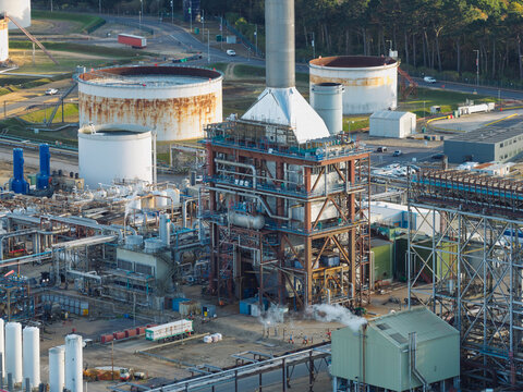 Aerial view of an oil refinery featuring a central processing tower, large storage tanks, and complex piping infrastructure in the United Kingdom.