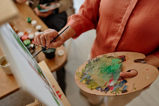 Senior woman painting on canvas holding wooden palette in art class. Concept representing active retirement and creative therapy for healthcare and community center promotion