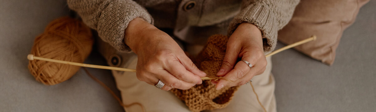 Senior woman knitting with wooden needles and yarn ball at community hobby club. Suitable for retirement leisure marketing, elderly craft workshop promotion, close up