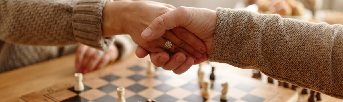 Cropped hands of senior people shaking hands over chessboard in community club. Ideal for retirement activities and elderly partnership marketing