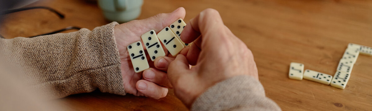 Senior man holding domino tiles during board game playing with Asian peers in community club. Image suitable for elderly care, leisure, retirement lifestyle promotion