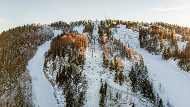 Aerial view of Col de la Faucille ski resort featuring snow-covered slopes, pine forests, and ski lifts under golden hour light in Gex, Auvergne-Rhone-Alpes, France.