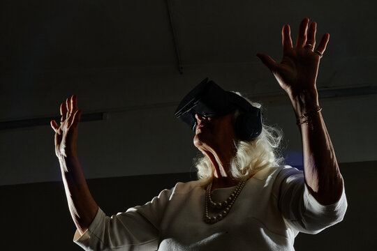 Senior Caucasian woman using VR headset and headphones with raised hands in club activity. Visual concept represents modern digital technology adoption for elderly care campaigns