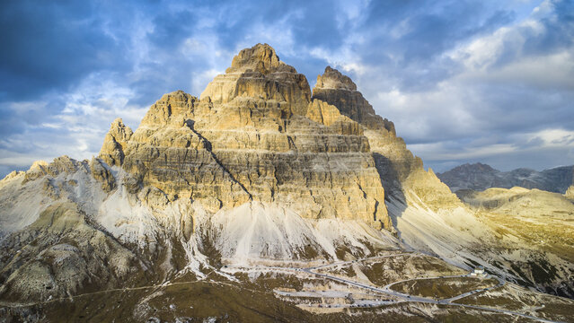 Aerial view of the Tre Cime di Lavaredo peaks in the Dolomites, with rugged limestone rock faces, scree slopes, and winding mountain roads, Tre Cime di Lavaredo, Veneto, Italy.