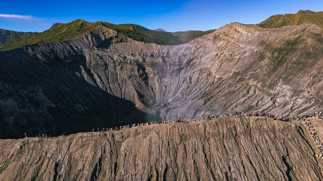 Aerial view of Mount Bromo crater with rugged volcanic slopes and people walking along the ridge in Tosari, East Java, Indonesia.