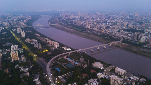 Aerial view of the Tapi River flowing through the city of Surat, featuring bridges, urban infrastructure, and residential buildings under a soft twilight sky in Surat, Gujarat, India.