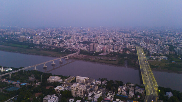 Aerial view of the cityscape of Surat along the Tapi River with bridges and urban architecture under a twilight sky in Surat, Gujarat, India.