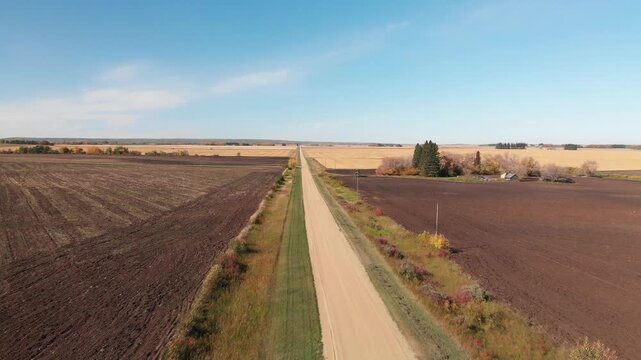 Drone flying above a straight gravel country road surrounded by recently ploughed fields
