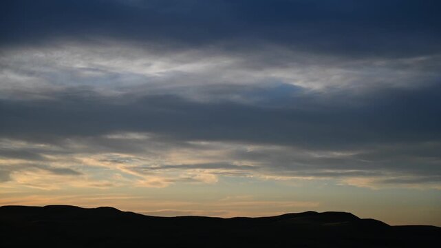 Time lapse of late day  sunset clouds moving above rolling prairie hills
