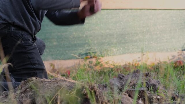 A man swings an axe to chop through thick tree roots that prevent a stump from being removed from the ground. 