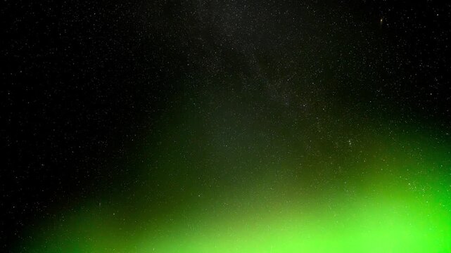 Night sky time lapse of a star filled sky with rotating stars and Aurora along the horizon
