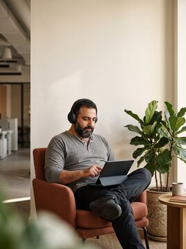 Man with headphones taking online course on tablet in office lounge armchair
