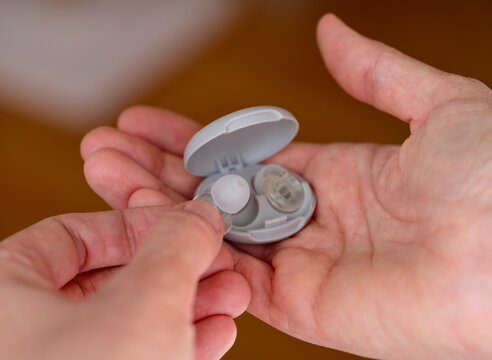 A close-up shot of woman hands holding an open grey plastic case and taking out a transparent silicone earplug.