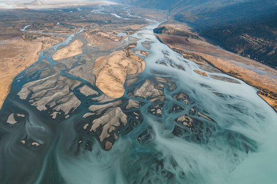 Aerial view of the braided channels of the Knik River with silt-laden glacial water flowing through the autumn landscape in Knik River, Alaska, United States.