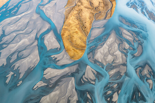 Aerial view of the Knik River with its braided glacial channels, vibrant turquoise water, and golden sediment banks in Knik River, Alaska, United States.