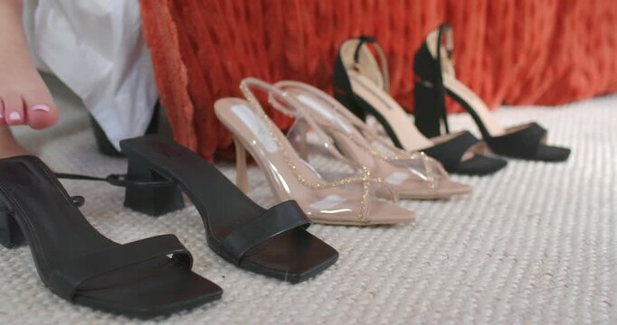 Heels sitting on carpet beside bed with barefoot reaching from left testing front mule to choose
