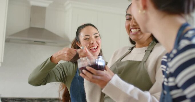 Diverse female friends center woman offering spoon urging woman testing mix in kitchen glass bowl