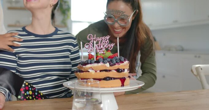 Diverse female friends placing HAPPY sash on woman with tiara, striped top by lit cake candles