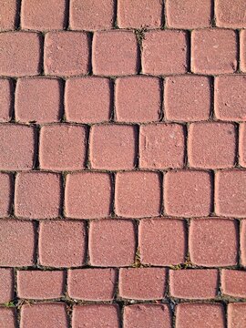 Seamless background texture of reddish brown rectangular interlocking concrete paving blocks on a city sidewalk.