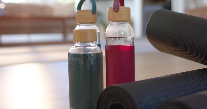 Camera is pulling back, revealing glass bottles with silicone loops and black mats for home workout