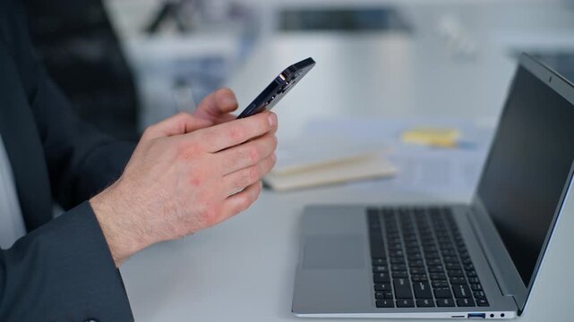 Cropped view unrecognizable business man using mobile phone at table with laptop work pause break in office male businessman worker using smartphone messaging online at desk with computer in company