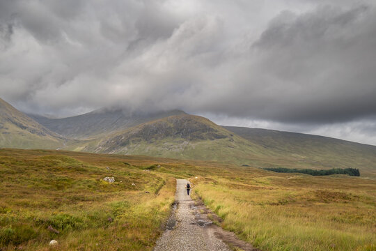 Hiker walking the West Highland Way on Rannoch Moor in the highlands of Scotland with Meall a' Bhuiridh mountain covered in cloud in the distance