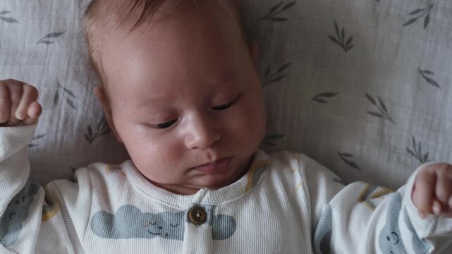 Hungry baby waiting for feeding, newborn in white sleepsuit lying on grey sheet looking down. Breastfeeding and baby formula concept, infant moves lips and looks down
