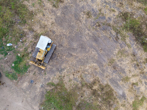 Aerial view of a yellow bulldozer parked on a dirt field with visible tire tracks in Indonesia.