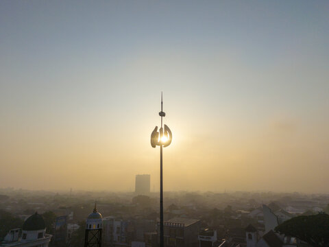 Aerial view of a mosque minaret spire silhouetted against the golden sunrise over the city rooftops in Malang, East Java, Indonesia.