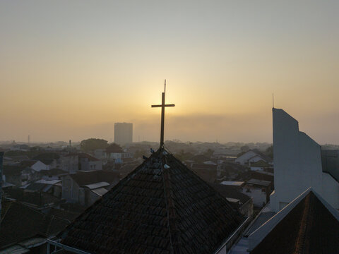 Aerial view of a church steeple with a cross at sunset overlooking the city rooftops in Malang, East Java, Indonesia.