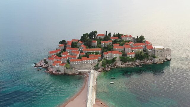 Honeymoon destination in Adriatic, aerial view of Sveti Stefan island with sandy causeway in turquoise water, Montenegro. Romantic travel concept, drone moves away from island