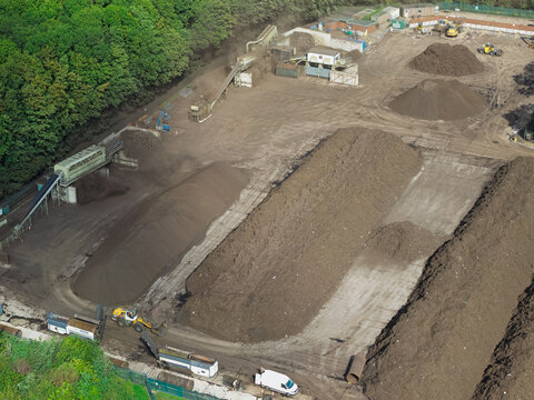 Aerial view of a biogas and composting facility featuring large piles of organic waste, conveyor belts, and heavy machinery operating on site in the United Kingdom.