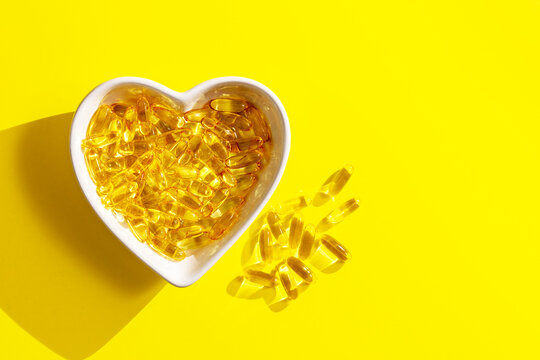 Omega 3 capsules in heart shape bowl on yellow background. Fish oil softgels or vitamin D supplement food, brain and heart health