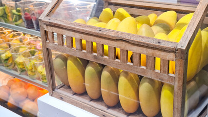 fresh ripe yellow mangoes displayed in wooden showcase with glass panel at fruit stall or market counter  © Rungphailin