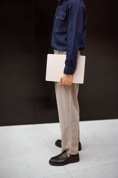 Person Stands in a Modern Space Holding a Laptop With One Hand