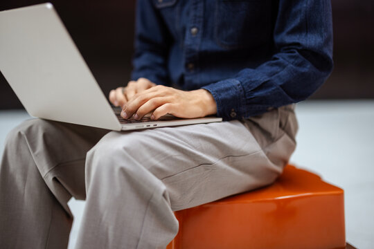 Person Using Laptop While Sitting on an Orange Stool