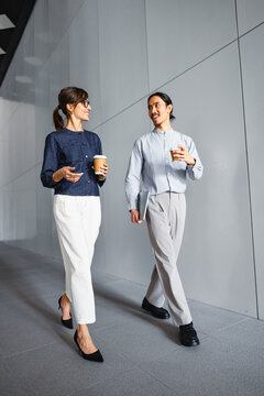 Two Colleagues Walk and Talk in a Modern Building Hallway